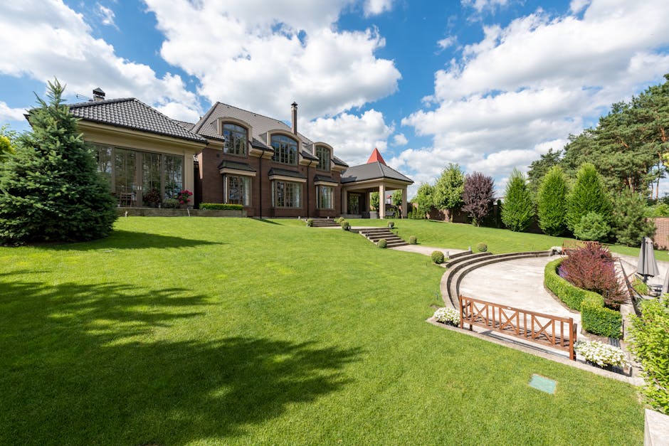 A spacious, well-maintained garden with a lush, green lawn and neatly trimmed edges, fronting a large, modern terraced home with a dark tiled roof and large windows. The garden features a gently slopi